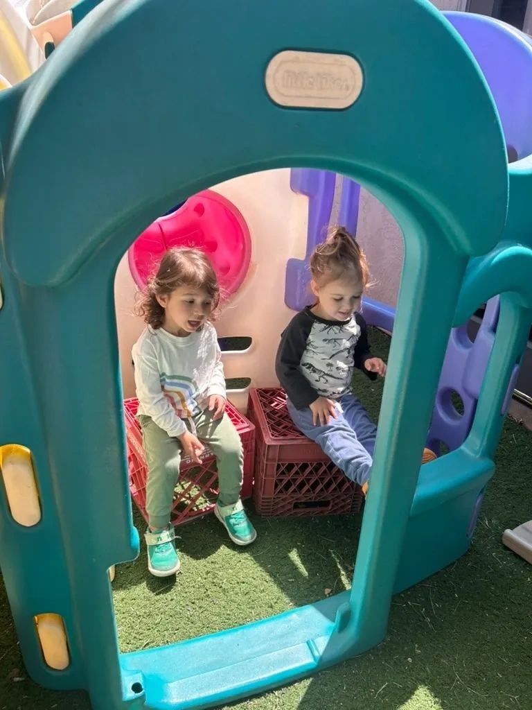 Two toddlers playing inside a colorful playhouse